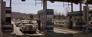 Movie still from “BUtterfield 8” (1960), directed by Daniel Mann – A man standing next to a car at a toll booth; Wide shot, High angle