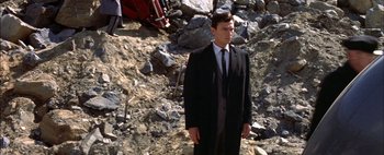 Movie still from “BUtterfield 8” (1960), directed by Daniel Mann – A man in a suit and tie standing in front of rocks; Medium shot, High angle