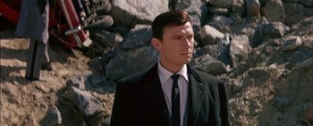 Movie still from “BUtterfield 8” (1960), directed by Daniel Mann – A man wearing a suit and tie standing in front of a rock wall; Close Up shot, Low angle