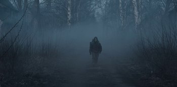 Movie still from “Dark” (2017), created by Baran bo Odar – A man walking through a foggy forest on a path; Wide shot, Low angle