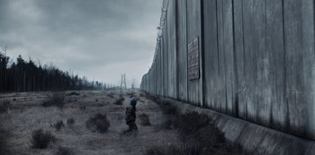 Movie still from “Dark” (2017), created by Baran bo Odar – A person standing next to a fence in a field; Extreme Wide shot, Low angle