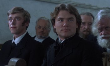 Movie still from “Babette's Feast” (1987), directed by Gabriel Axel – A man in a suit and tie with a bunch of other men in the background; Close Up shot, Over the shoulder angle