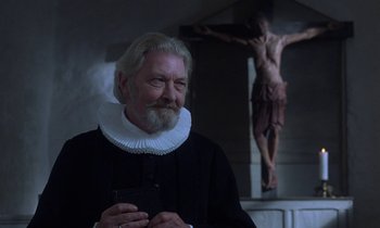 Movie still from “Babette's Feast” (1987), directed by Gabriel Axel – An old man with a beard and a white beard is standing in front of a crucifixion; Medium shot, Low angle