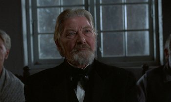 Movie still from “Babette's Feast” (1987), directed by Gabriel Axel – An old man with a beard wearing a black suit and bow tie; Close Up shot, Low angle
