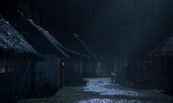 Movie still from “Babette's Feast” (1987), directed by Gabriel Axel – A person standing in the rain next to a building; Extreme Wide shot, High angle