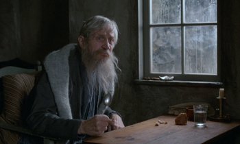 Movie still from “Babette's Feast” (1987), directed by Gabriel Axel – An old man sitting at a wooden table; Medium shot, High angle