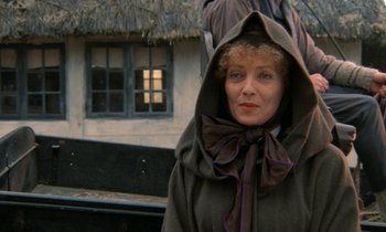 Movie still from “Babette's Feast” (1987), directed by Gabriel Axel – A woman wearing a hooded cloak standing in front of a house; Close Up shot, Over the shoulder angle