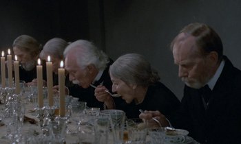 Movie still from “Babette's Feast” (1987), directed by Gabriel Axel – A group of people sitting at a dinner table eating food; Wide shot, High angle