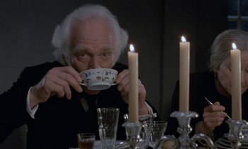 Movie still from “Babette's Feast” (1987), directed by Gabriel Axel – An old man sitting at a dinner table drinking from a tea cup; Close Up shot, High angle