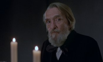 Movie still from “Babette's Feast” (1987), directed by Gabriel Axel – An old man with a long white beard is looking at a candle; Close Up shot, Over the shoulder angle