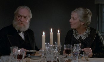 Movie still from “Babette's Feast” (1987), directed by Gabriel Axel – A man and a woman sitting at a dinner table with lit candles; Close Up shot, Over the shoulder angle