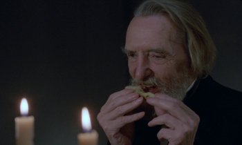 Movie still from “Babette's Feast” (1987), directed by Gabriel Axel – An older man eating a piece of bread by a candle; Close Up shot, High angle