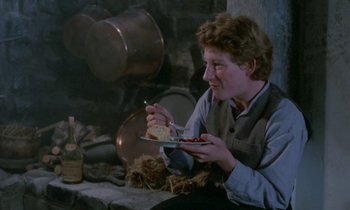 Movie still from “Babette's Feast” (1987), directed by Gabriel Axel – A man sitting in front of a fireplace holding a plate of food; Medium shot, Over the shoulder angle