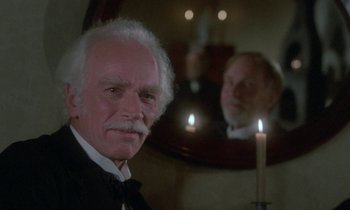 Movie still from “Babette's Feast” (1987), directed by Gabriel Axel – An older man in a suit and tie in front of a mirror; Close Up shot, Over the shoulder angle