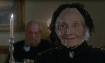 Movie still from “Babette's Feast” (1987), directed by Gabriel Axel – An old woman wearing a black dress and a black hat; Close Up shot, Over the shoulder angle