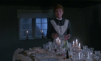 Movie still from “Babette's Feast” (1987), directed by Gabriel Axel – A woman standing in front of a table filled with wine glasses; Medium shot, Over the shoulder angle