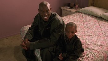 Movie still from “Baby Boy” (2001), directed by John Singleton – A man and a boy sitting on a bed; Medium shot, High angle
