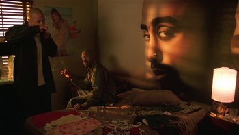 Movie still from “Baby Boy” (2001), directed by John Singleton – A man sitting on top of a bed in front of a mural of tupac shakur; Medium shot, High angle