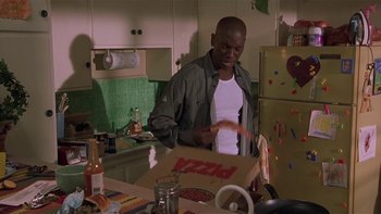 Movie still from “Baby Boy” (2001), directed by John Singleton – A man standing in front of an open box of pizza; Medium shot, High angle