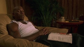 Movie still from “Baby Boy” (2001), directed by John Singleton – A man laying on a couch reading a newspaper; Medium shot, High angle