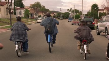Movie still from “Baby Boy” (2001), directed by John Singleton – A man riding a bike down the middle of a street; Wide shot, High angle