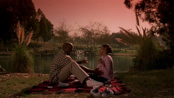 Movie still from “Baby Boy” (2001), directed by John Singleton – A man and a woman sitting on a blanket near a body of water; Wide shot, High angle