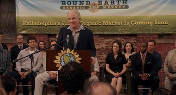 Movie still from “Baby Mama” (2008), directed by Michael McCullers – A man is giving a speech in front of a group of people; Medium shot, Over the shoulder angle