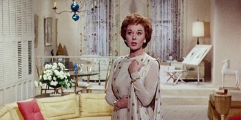 Movie still from “Back Street” (1961), directed by David Miller – A woman standing in a living room wearing a white dress; Medium shot, Low angle