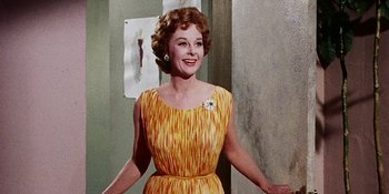 Movie still from “Back Street” (1961), directed by David Miller – An older woman wearing a yellow dress and smiling for the camera; Medium shot, Low angle