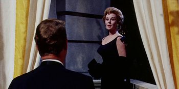 Movie still from “Back Street” (1961), directed by David Miller – A woman in a black dress talking to a man in a black suit; Medium shot, Over the shoulder angle