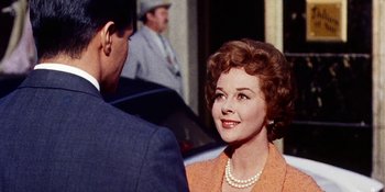 An older woman wearing a pearl necklace talking to an older man