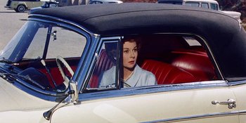 Movie still from “Back Street” (1961), directed by David Miller – A woman sitting in the driver's seat of an old car; Medium shot, High angle