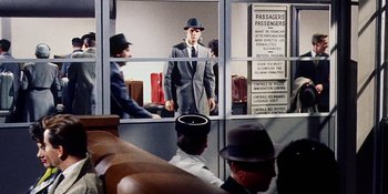 Movie still from “Back Street” (1961), directed by David Miller – A man in a suit and a hat in the window; Wide shot, Low angle