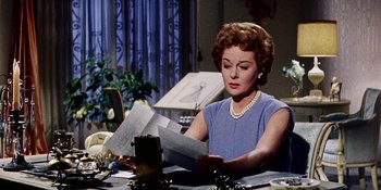 Movie still from “Back Street” (1961), directed by David Miller – An older woman sitting at a table reading a letter; Medium shot, Low angle