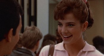 Movie still from “Back to School” (1986), directed by Alan Metter – A woman smiling for the camera while standing next to a group of people; Close Up shot, Over the shoulder angle