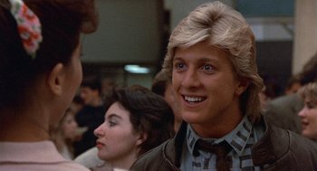 Movie still from “Back to School” (1986), directed by Alan Metter – A man with blonde hair is smiling for the camera; Close Up shot, Over the shoulder angle