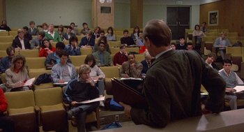 Movie still from “Back to School” (1986), directed by Alan Metter – A group of people sitting in front of a man holding papers; Wide shot, High angle