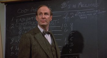 Movie still from “Back to School” (1986), directed by Alan Metter – A man standing in front of a blackboard with numbers on it; Close Up shot, Over the shoulder angle