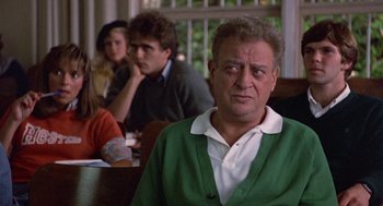 Movie still from “Back to School” (1986), directed by Alan Metter – An older man in a green sweater is looking at the camera; Close Up shot, Over the shoulder angle