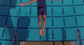 Movie still from “Back to School” (1986), directed by Alan Metter – A man in blue shorts is diving in a pool; Wide shot, Overhead angle