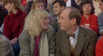 Movie still from “Back to School” (1986), directed by Alan Metter – A man and a woman sitting next to each other in a crowd; Close Up shot, Over the shoulder angle