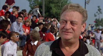 Movie still from “Back to School” (1986), directed by Alan Metter – A man standing in front of a group of people; Close Up shot, Over the shoulder angle