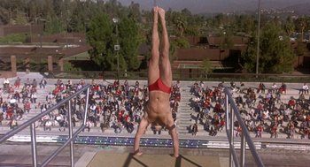 Movie still from “Back to School” (1986), directed by Alan Metter – A man doing a handstand on a railing in front of a crowd; Wide shot, Overhead angle