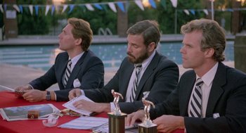 Movie still from “Back to School” (1986), directed by Alan Metter – A group of men sitting at a table with trophies; Medium shot, Low angle