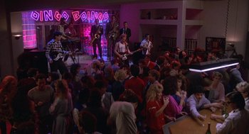Movie still from “Back to School” (1986), directed by Alan Metter – A group of people standing around a room with lights on; Wide shot, High angle