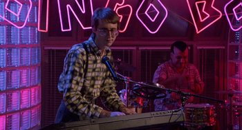 Movie still from “Back to School” (1986), directed by Alan Metter – A man playing a keyboard in front of a microphone; Medium shot, Low angle