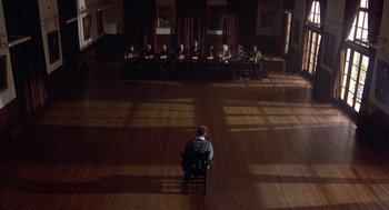 Movie still from “Back to School” (1986), directed by Alan Metter – A group of people sitting at a table in front of a man; Extreme Wide shot, High angle