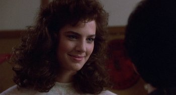 Movie still from “Back to School” (1986), directed by Alan Metter – A young woman with long hair smiling for the camera; Close Up shot, Over the shoulder angle