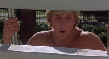 Movie still from “Back to School” (1986), directed by Alan Metter – A shirtless man looking through a fence; Close Up shot, Low angle