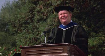 Movie still from “Back to School” (1986), directed by Alan Metter – A man wearing a graduation cap and gown standing in front of a podium; Medium shot, Low angle